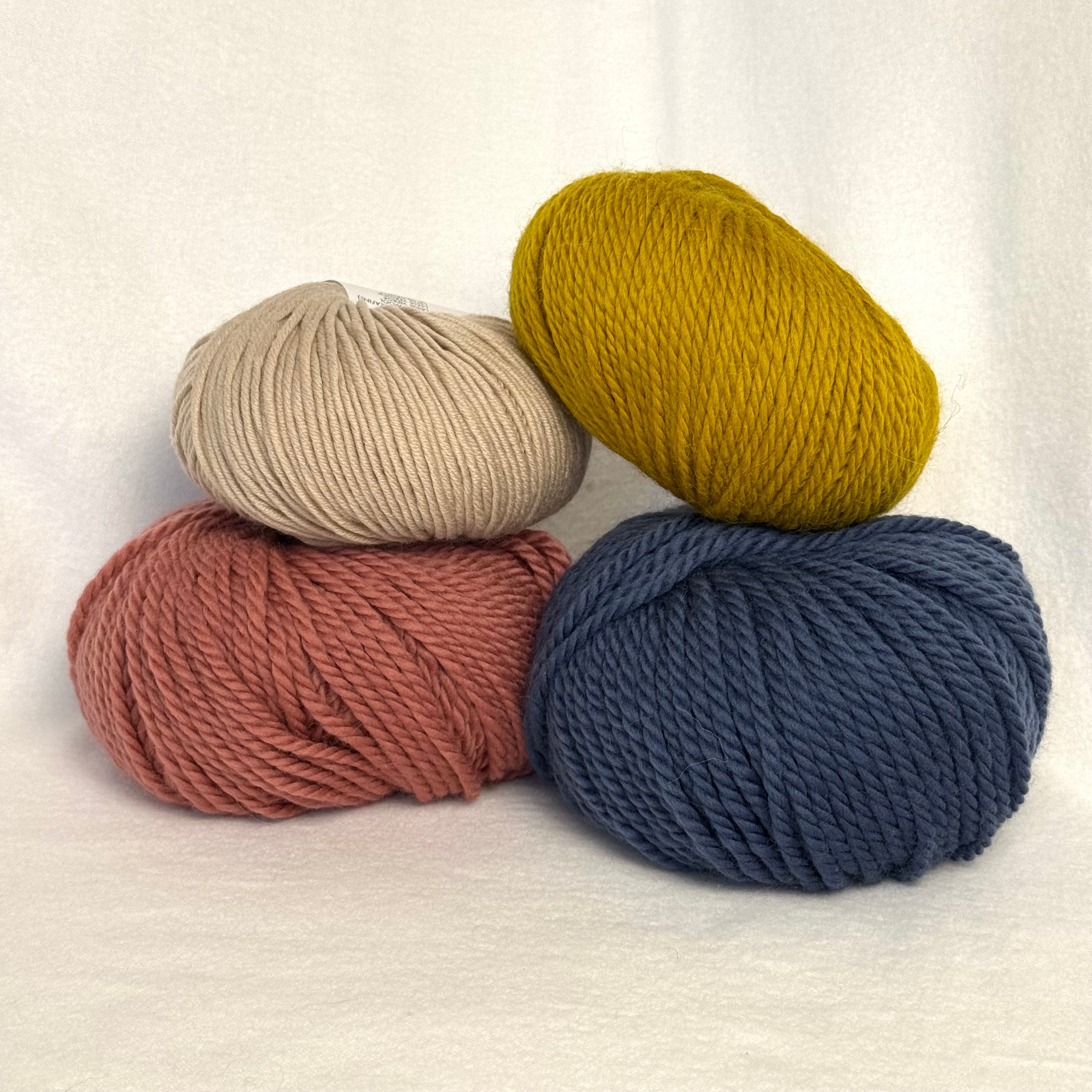 Four balls of yarn in beige, green, brown, and blue on a white background
